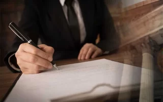 حق تقدم در مرحله اجرای احکام مدنی چگونه رعایت می شود؟| وکیلی درحال نوشتن روی برگه که پشت زمینه ستون های نمای دادگاه دیده مشود