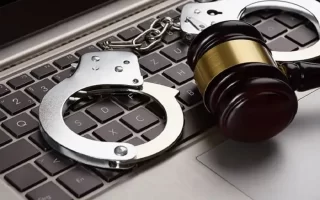 وکیل کلاهبرداری اینترنتی| دستبند زندانیان و المان حقوقی چکش روی کیبورد کامپیوتر